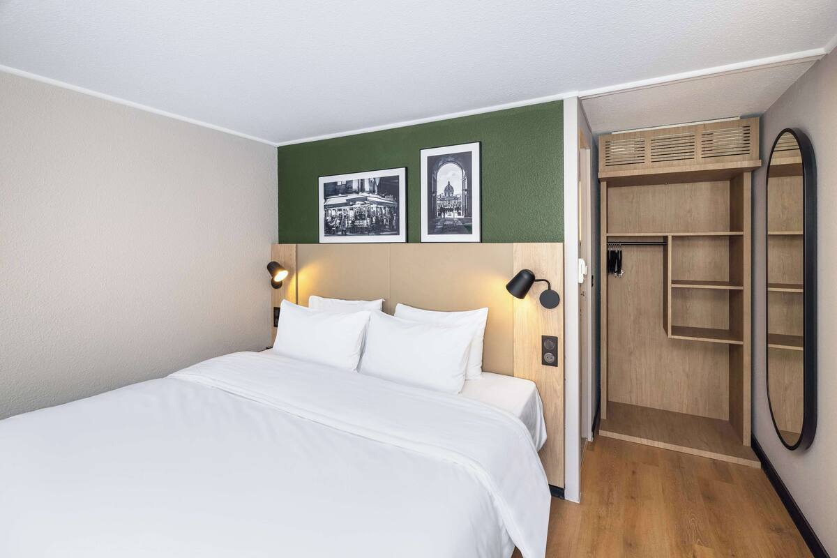 A neatly made bed with white linens, a green accent wall, and two black-framed wall sconces.