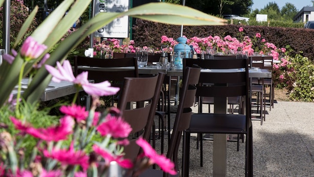 An outdoor dining area with tables and chairs, surrounded by flowers and greenery. - Campanile NATURE - Cergy Saint Christophe (Osny)