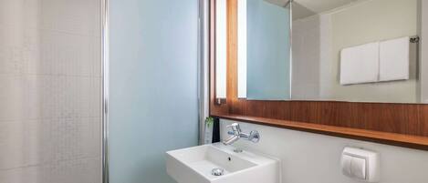 Un baño con cabina de ducha de vidrio, un lavabo blanco con encimera de madera y un espejo con marco de madera.