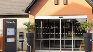 A building with a modern design, featuring a prominent 'A' logo on the facade, a water dispenser, and potted plants. - Campanile NATURE - Cergy Saint Christophe (Osny)