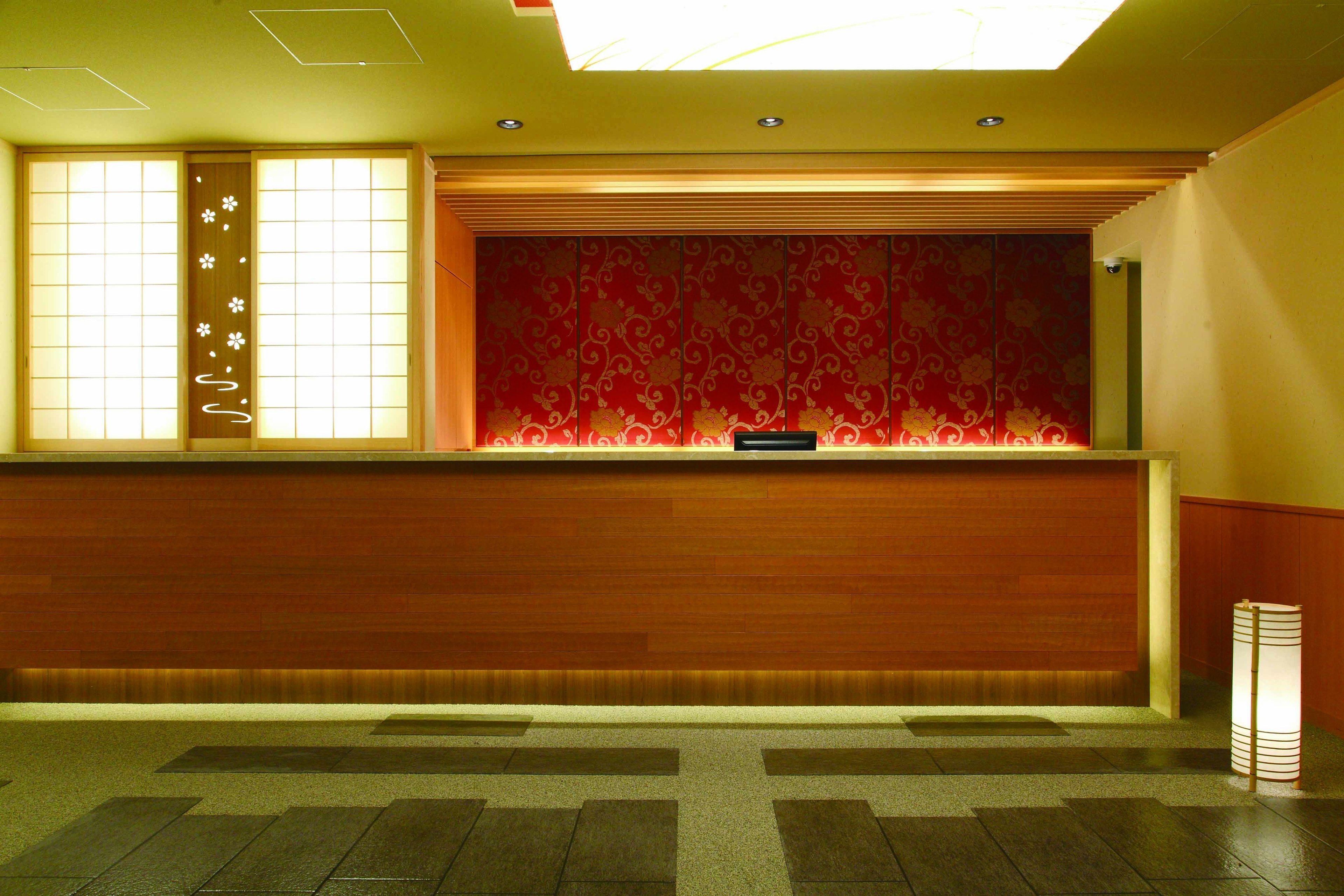A reception area with a wooden reception desk, a red patterned wall, and a traditional Japanese sliding door.