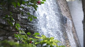 A waterfall cascading down a stone wall with a view of a building in the background. - Matsui Honkan (Kyoto)