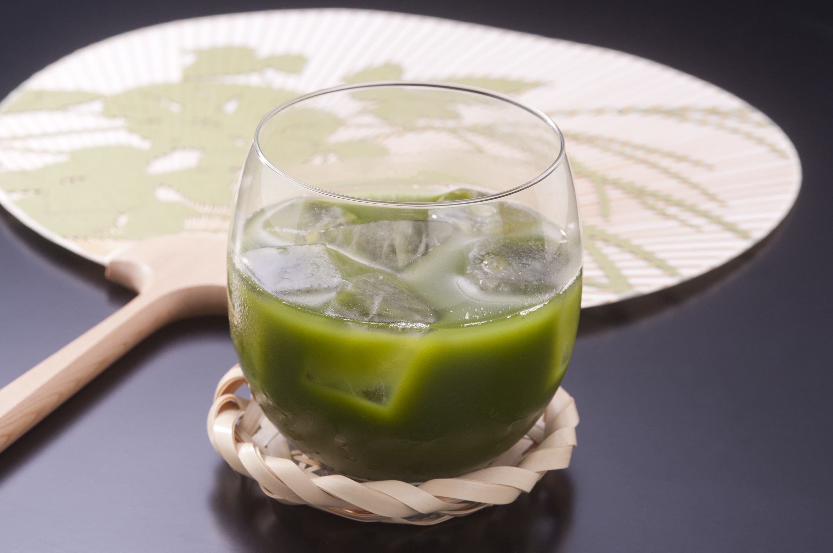 A glass of green beverage on a woven coaster.