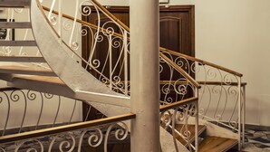 Una escalera de caracol con barandillas de metal ornamentadas y escalones de madera, que conduce a un piso superior con vistas al cielo a través de amplias ventanas.