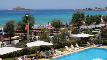 Un espace aménagé au bord de la piscine, avec des chaises longues, des parasols et des drapeaux.