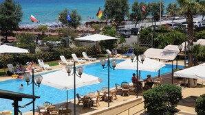Zona de piscina con sillones de descanso y sombrillas, vista al mar y banderas.