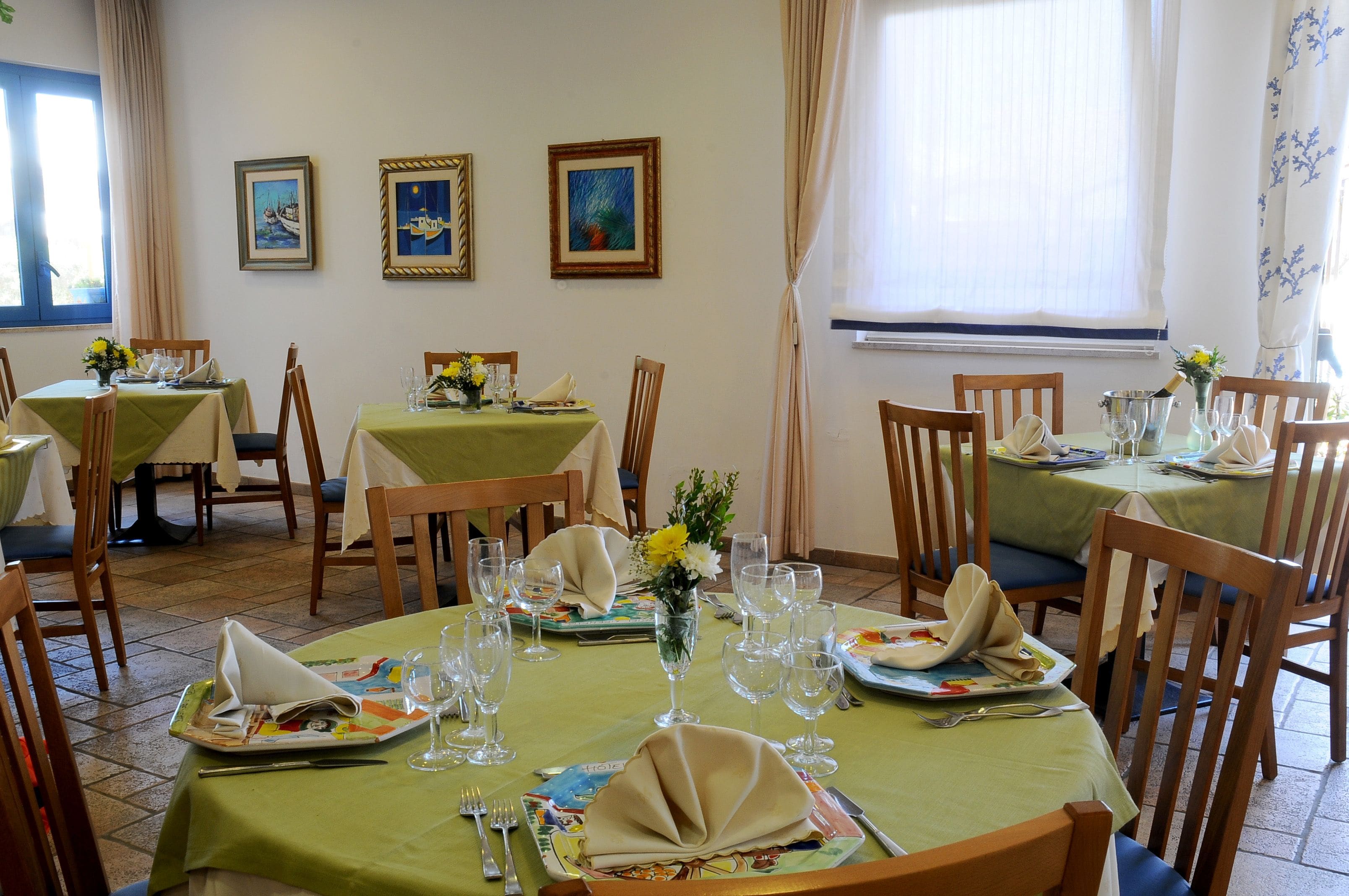 A dining area with tables set for a meal, chairs, and framed artwork on the walls.