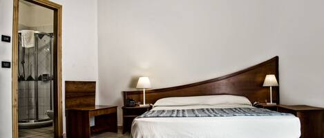 Habitación de hotel con cama, dos mesitas de noche, cabecero de madera, lámpara y espejo.