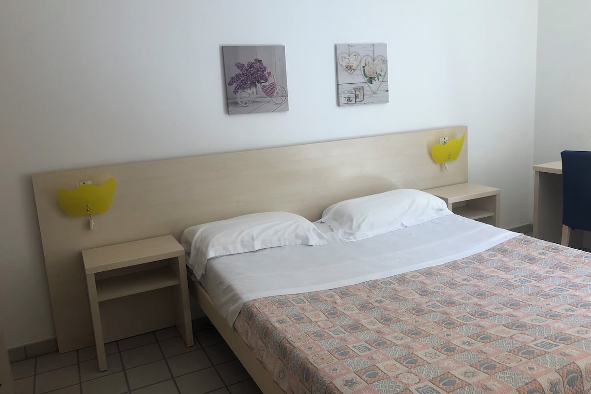 Una camera d'albergo con un letto, due comodini, una testiera e due decorazioni appese al muro.