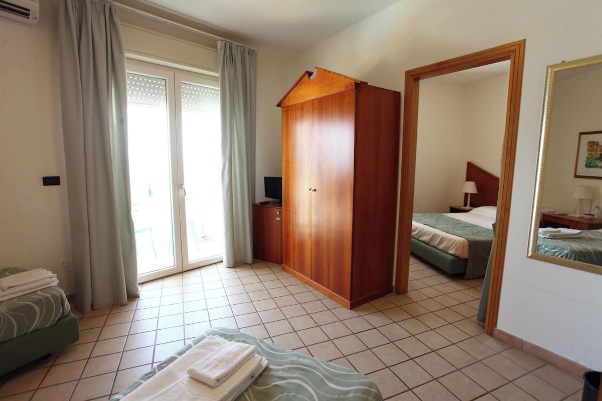 Una camera d'albergo con un letto, un armadio in legno, un bagno con doccia e un balcone con tende.