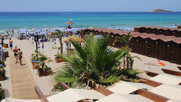 Un hotel frente a la playa con hileras de cabañas de madera, un paseo marítimo de madera y una vista despejada del mar.