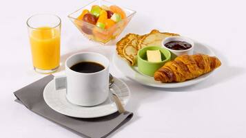 A breakfast setting with a glass of orange juice, a fruit bowl, a croissant, butter, jam, and a cup of coffee.