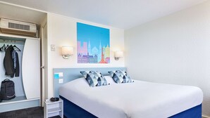 A hotel room with a large bed, a wardrobe, a coat rack, and a wall-mounted air conditioner. - Kyriad Direct Le Bourget - Gonesse (Gonesse)