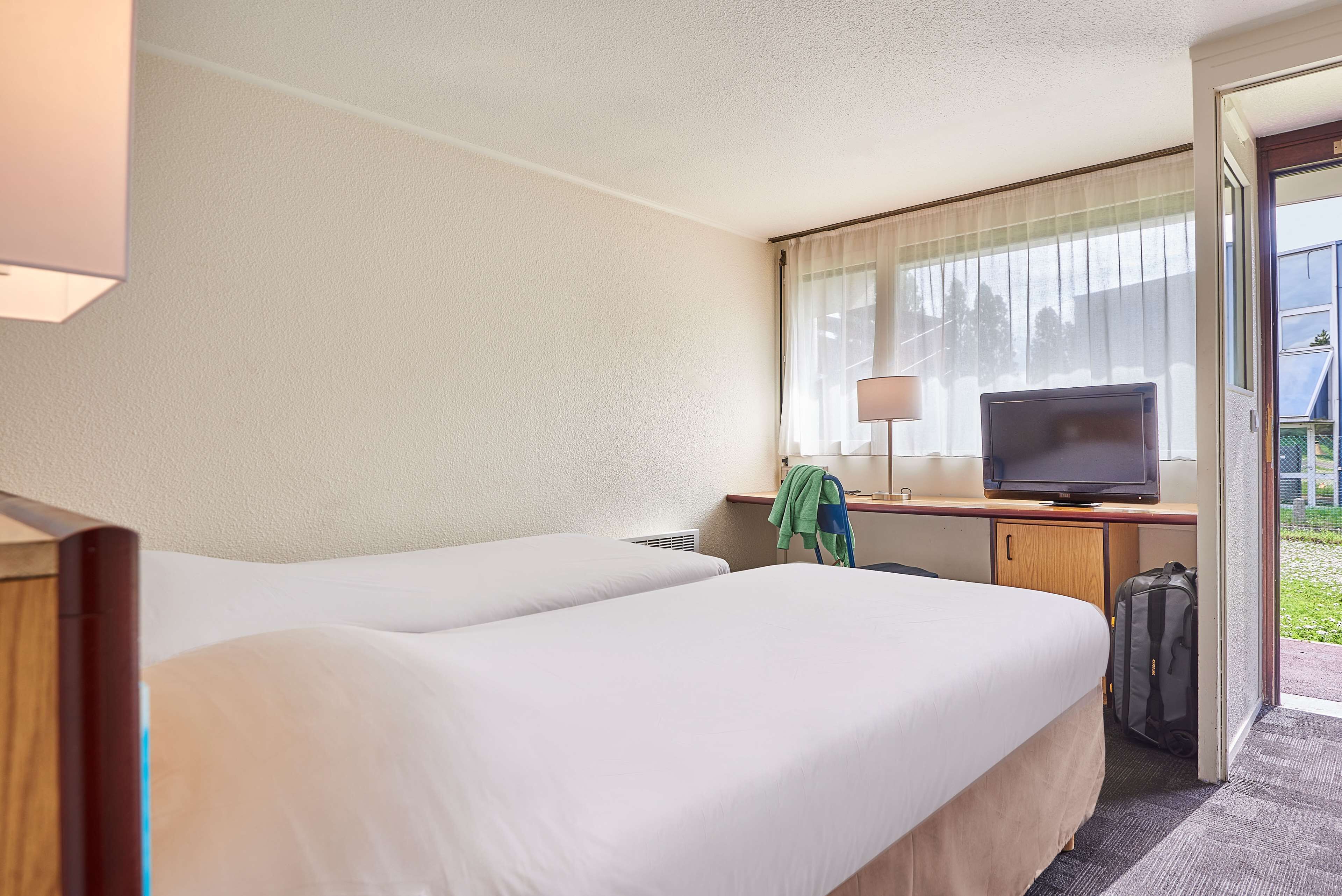 Una habitación de hotel con dos camas, un escritorio, un televisor, una lámpara y una maleta.
