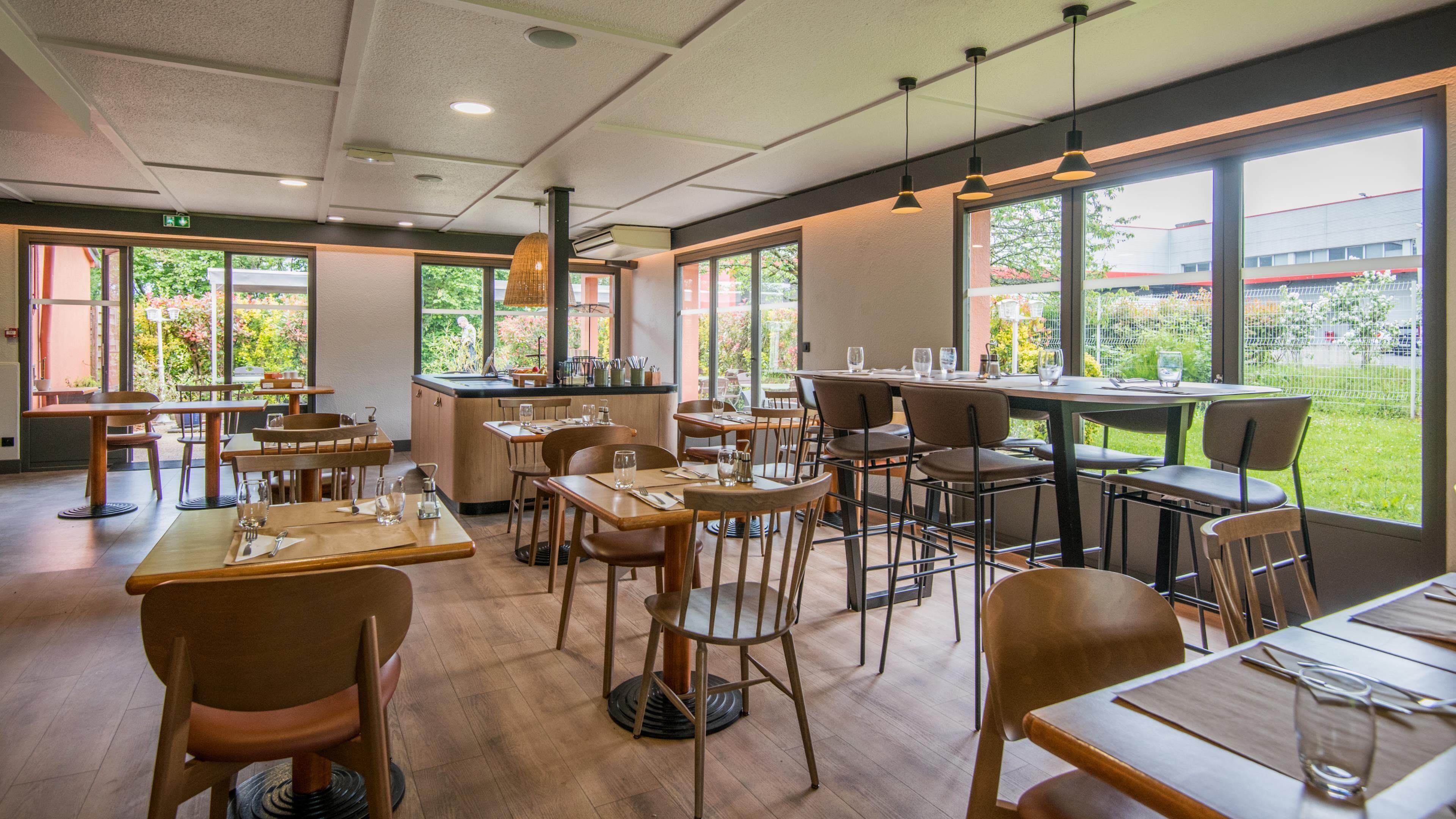 Un restaurante con mesas y sillas de madera, amplios ventanales y lámparas colgantes.