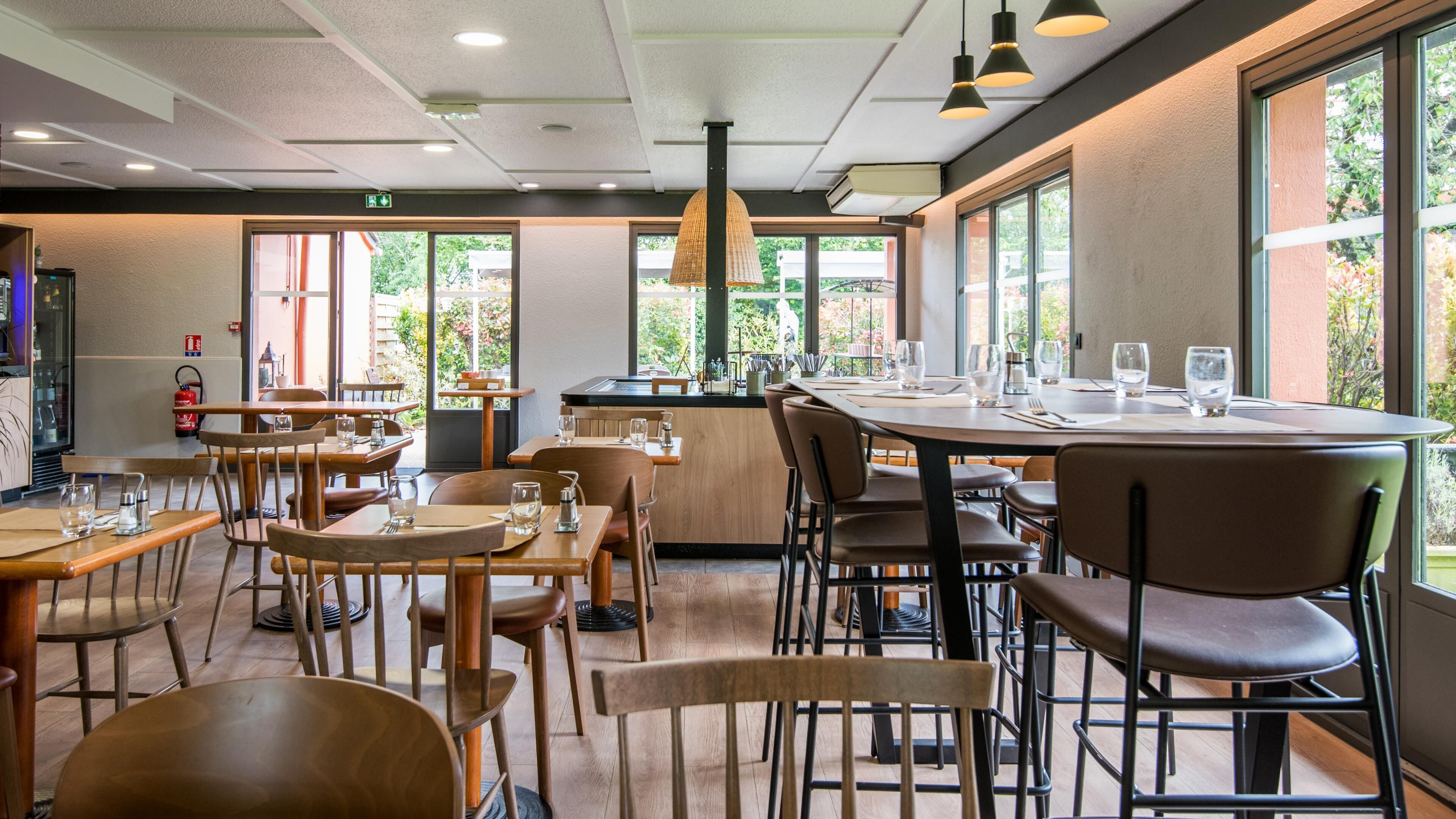 Un ristorante con diversi tavoli e sedie, un'area bar centrale e ampie finestre che offrono vista sull'esterno.