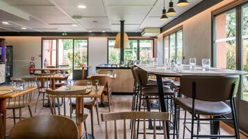 Un ristorante con diversi tavoli e sedie, un'area bar centrale e ampie finestre che offrono vista sull'esterno.