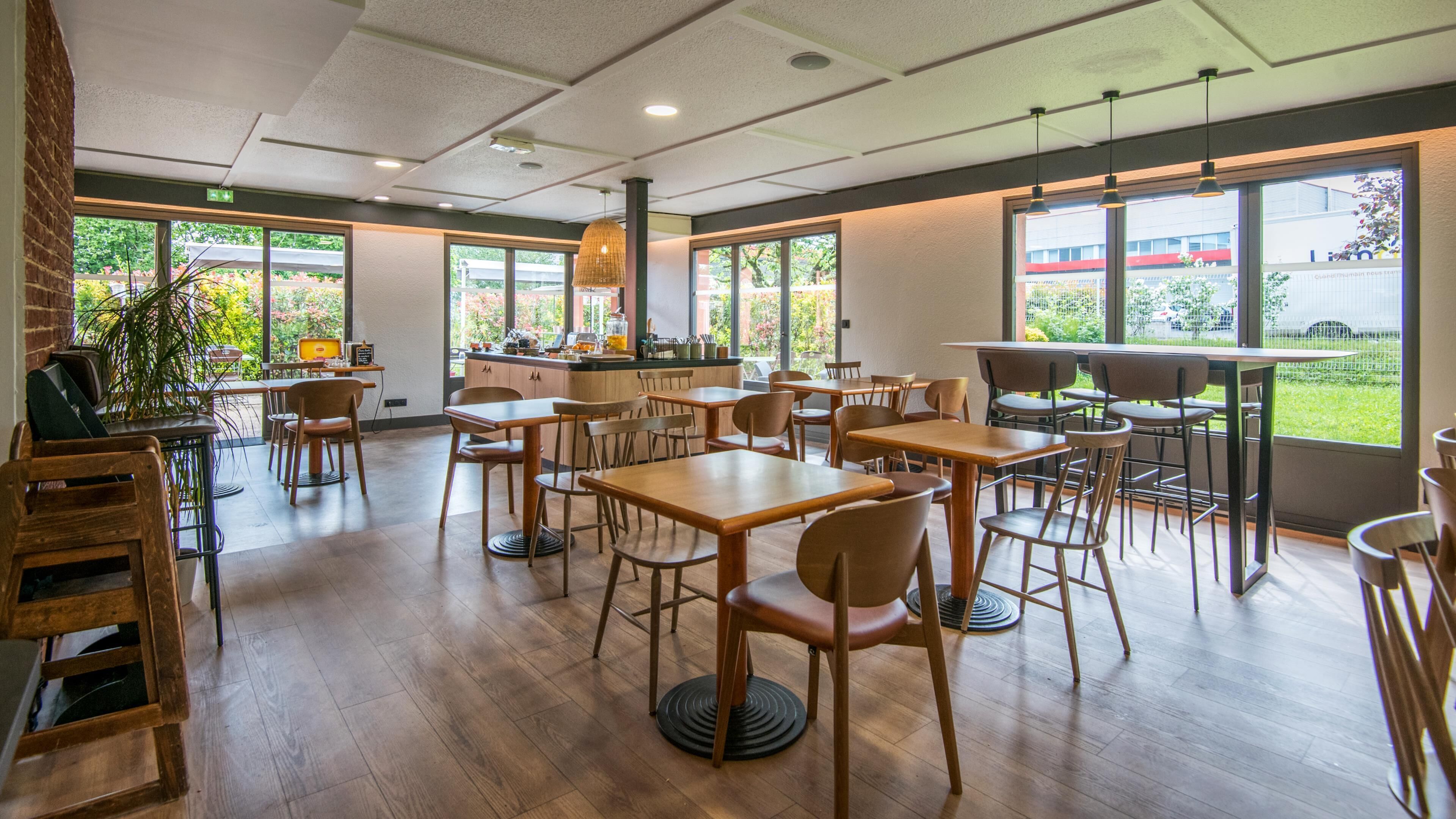 A restaurant with wooden tables and chairs, large windows, and a brick wall.