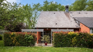 Une maison avec un toit en pente, une véranda et un jardin où poussent différentes plantes et fleurs.