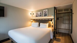 Una habitación de hotel con una cama grande, un televisor montado en la pared y un armario de madera.