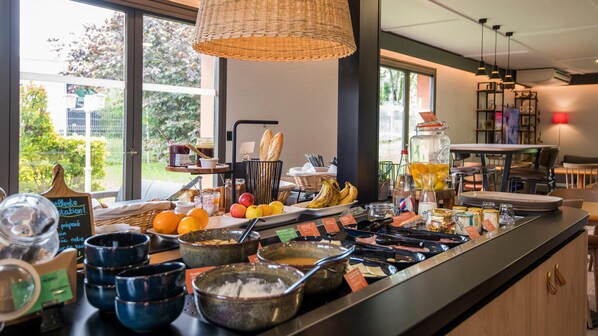 Un buffet proposant une variété de plats et de boissons, un luminaire suspendu en osier et une vue sur la verdure environnante.