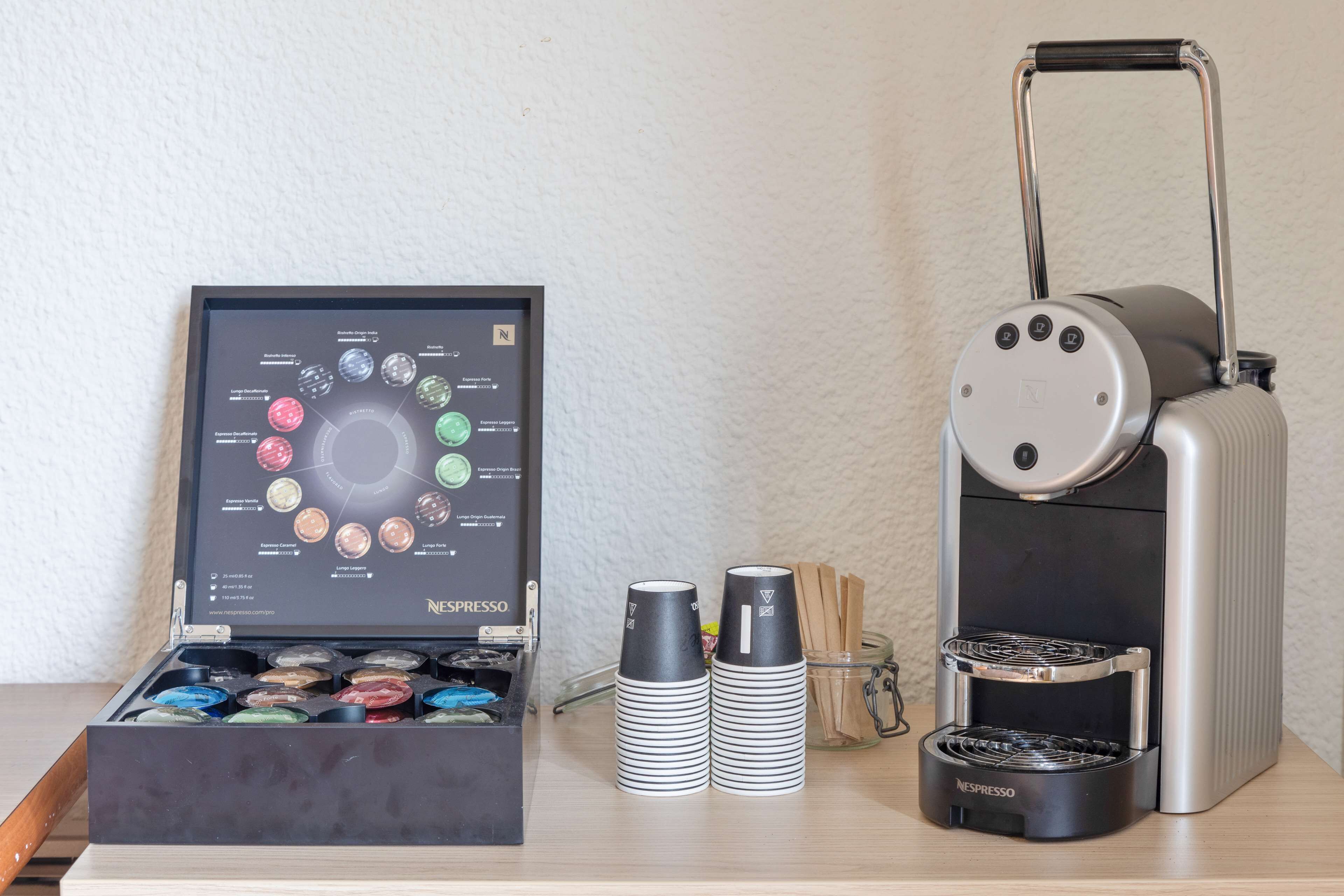 Eine Nespresso-Kaffeemaschine, eine Vorratsanzeige für Kaffeekapseln und ein Stapel Einwegbecher auf einem Tisch.