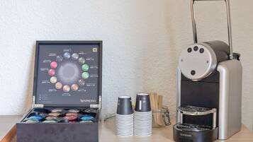 Eine Nespresso-Kaffeemaschine, eine Vorratsanzeige für Kaffeekapseln und ein Stapel Einwegbecher auf einem Tisch.