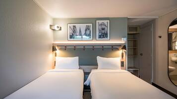 Een hotelkamer met twee bedden, een hoofdeinde met een lamp, twee ingelijste foto’s aan de muur, een nachtkastje en een zichtbare badkamer door een geopende deur.