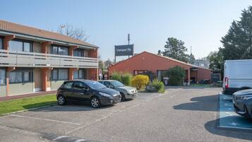 A parking lot with two cars, a building with a sign 'Campagne Nature,' and a van.
