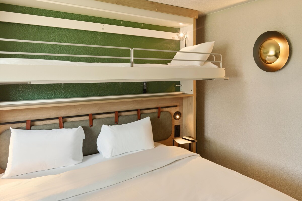 Un lit superposé avec une tête de lit en bois, une table de chevet avec une lampe et un luminaire fixé au mur.