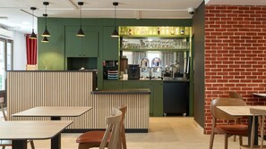Ein modernes Café mit Holztischen und -stühlen, einer grünen Theke mit einer Kaffeemaschine und einer Backsteinwand.