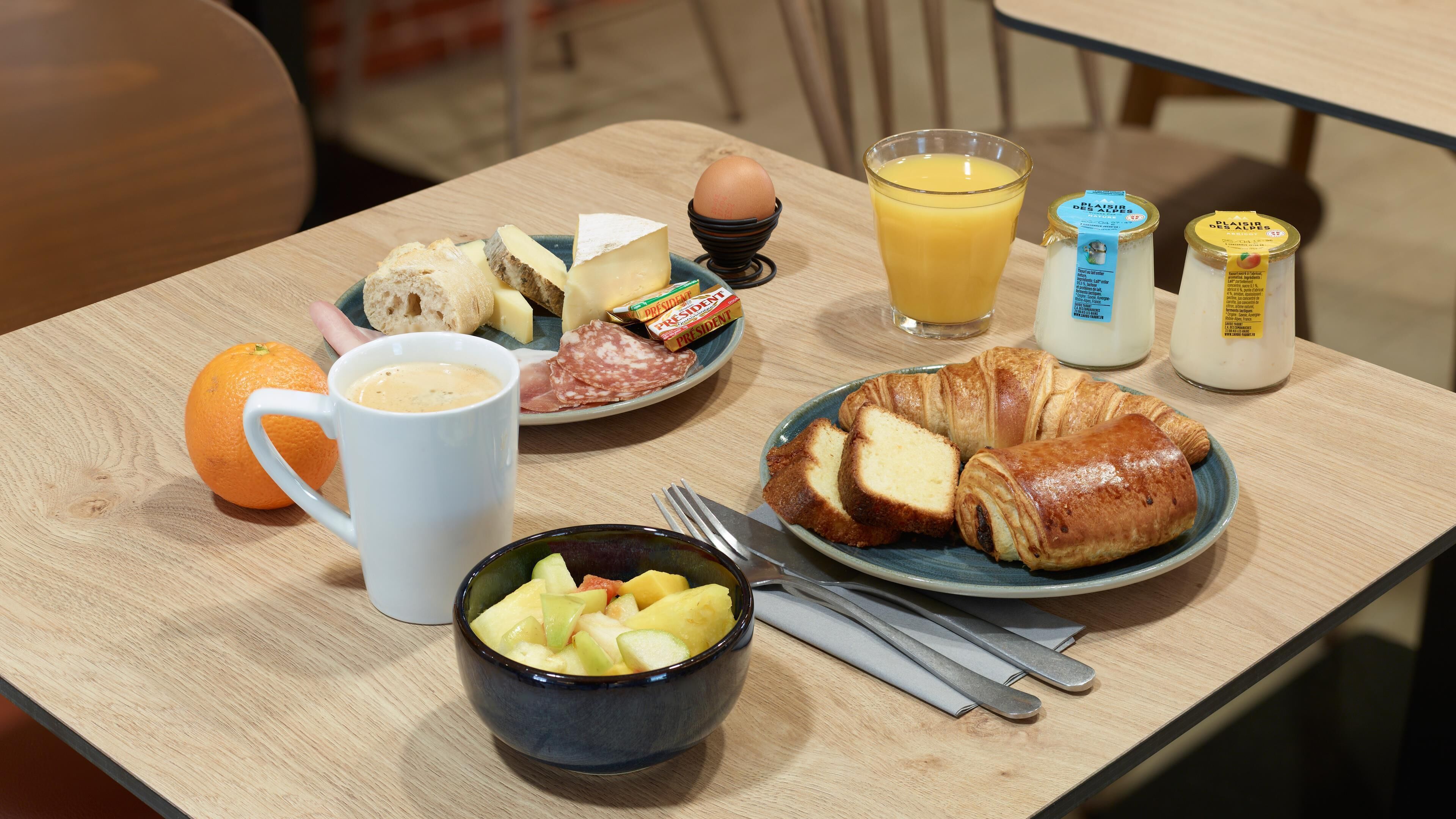 Een ontbijttafel met croissants, kaas, eieren, sinaasappelsap, melk en fruit.