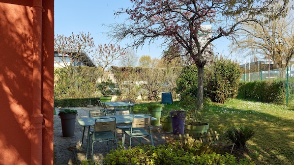 An outdoor seating area with tables and chairs, surrounded by greenery and trees.