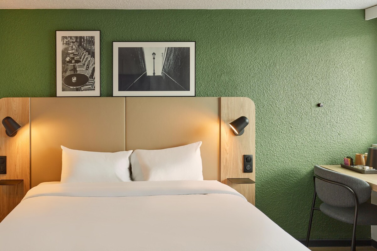 Une chambre d’hôtel avec un lit, un bureau et deux tableaux encadrés au mur.
