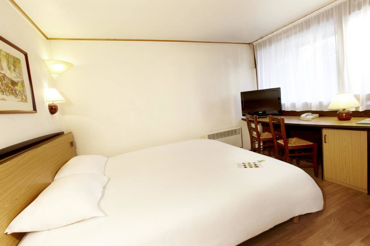 A hotel room with a bed, desk, chairs, and a television.