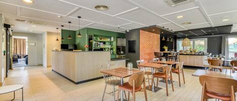 A modern restaurant with a bar area, wooden tables and chairs, and a green accent wall.