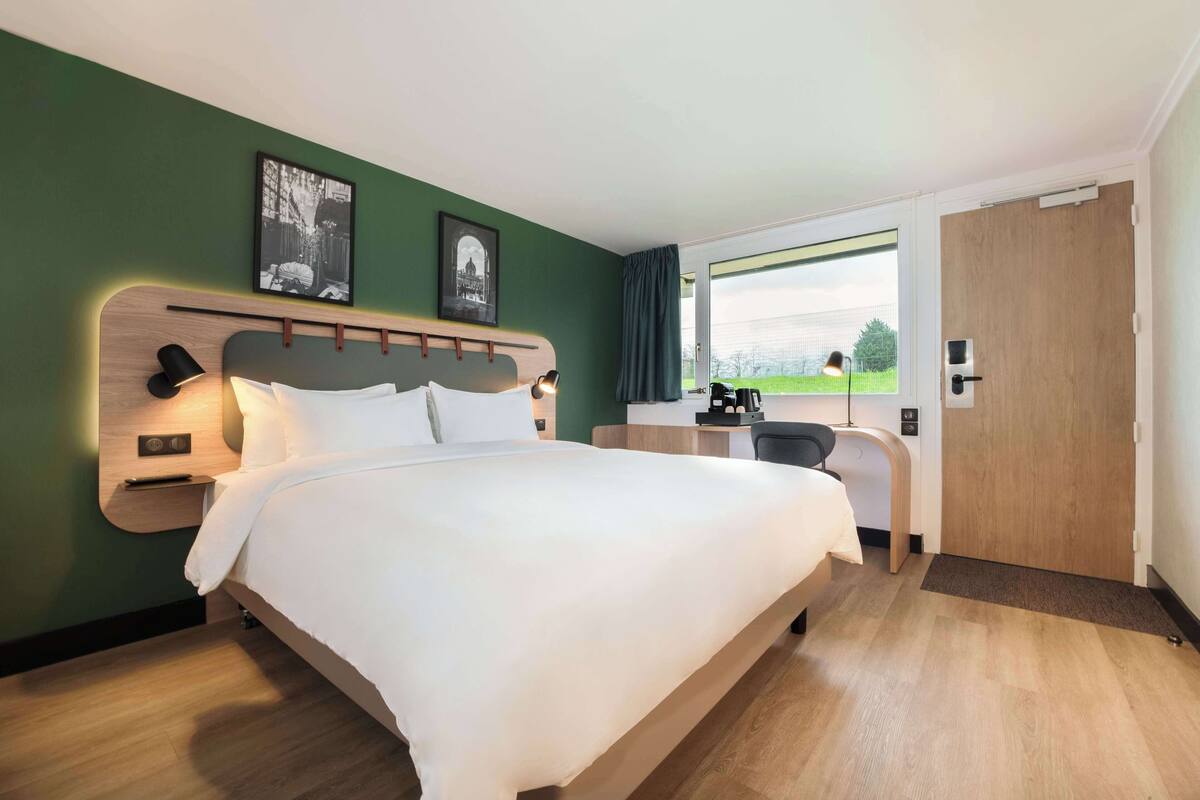Habitación de hotel con una cama grande, un escritorio, una silla y una ventana con vistas al exterior.