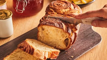On voit une miche de pain qu’on tranche sur une planche à découper en bois à l’aide d’un couteau.
