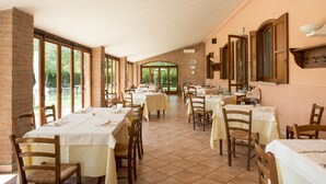 Un comedor amplio con varias mesas y sillas, ventanas grandes y una pared de ladrillo.