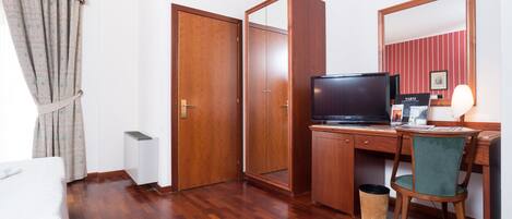 Una habitación de hotel con suelo de madera, un escritorio con computadora, televisor y espejo.