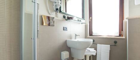 A bathroom with a glass shower enclosure, a white sink, a mirror, and a window.