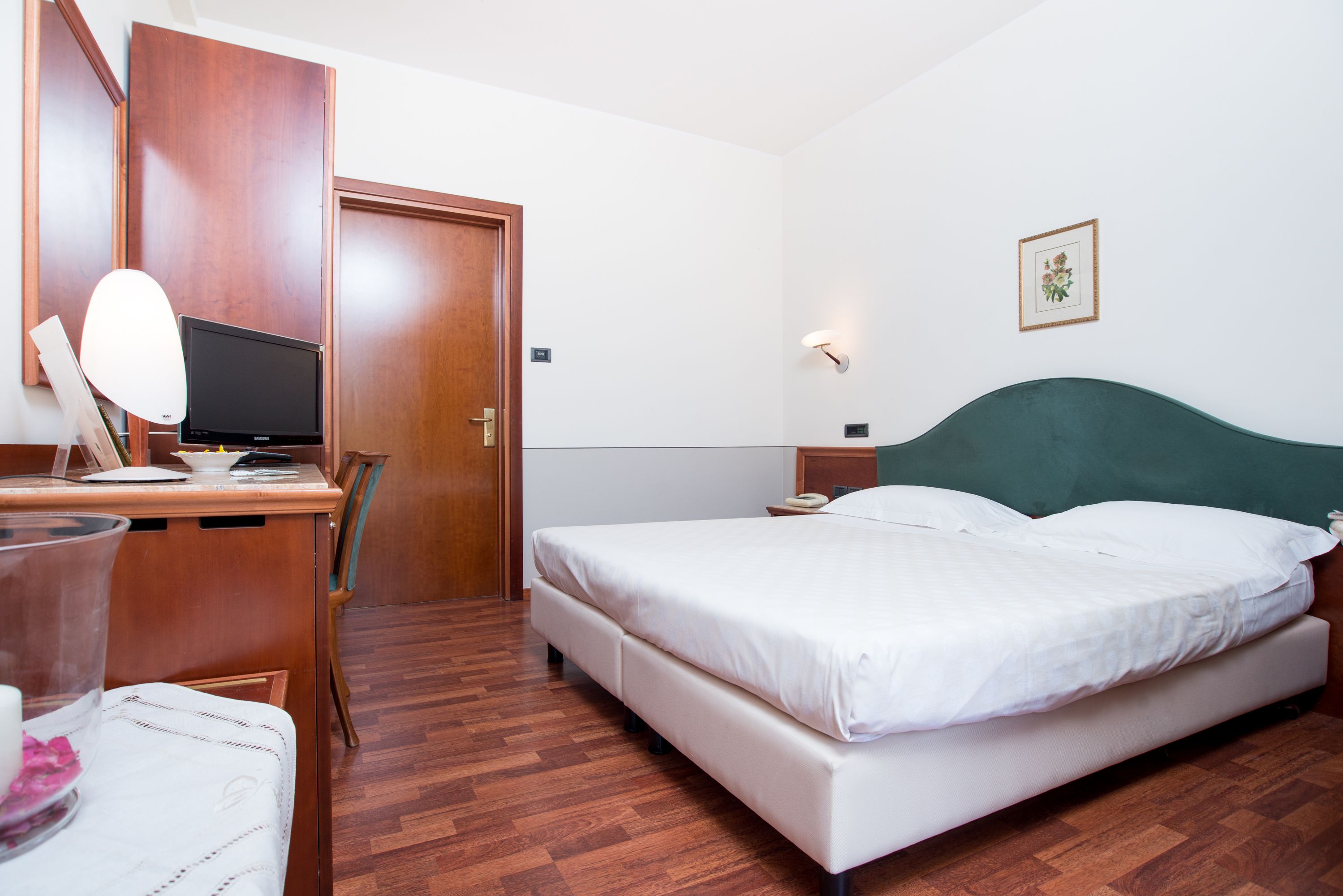 A hotel room with a wooden desk, a bed, a chair, and a bedside table.