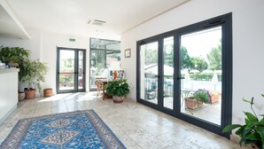 Un hall de hotel espacioso con un suelo estampado, plantas en macetas y vistas al exterior a través de amplias puertas de cristal.