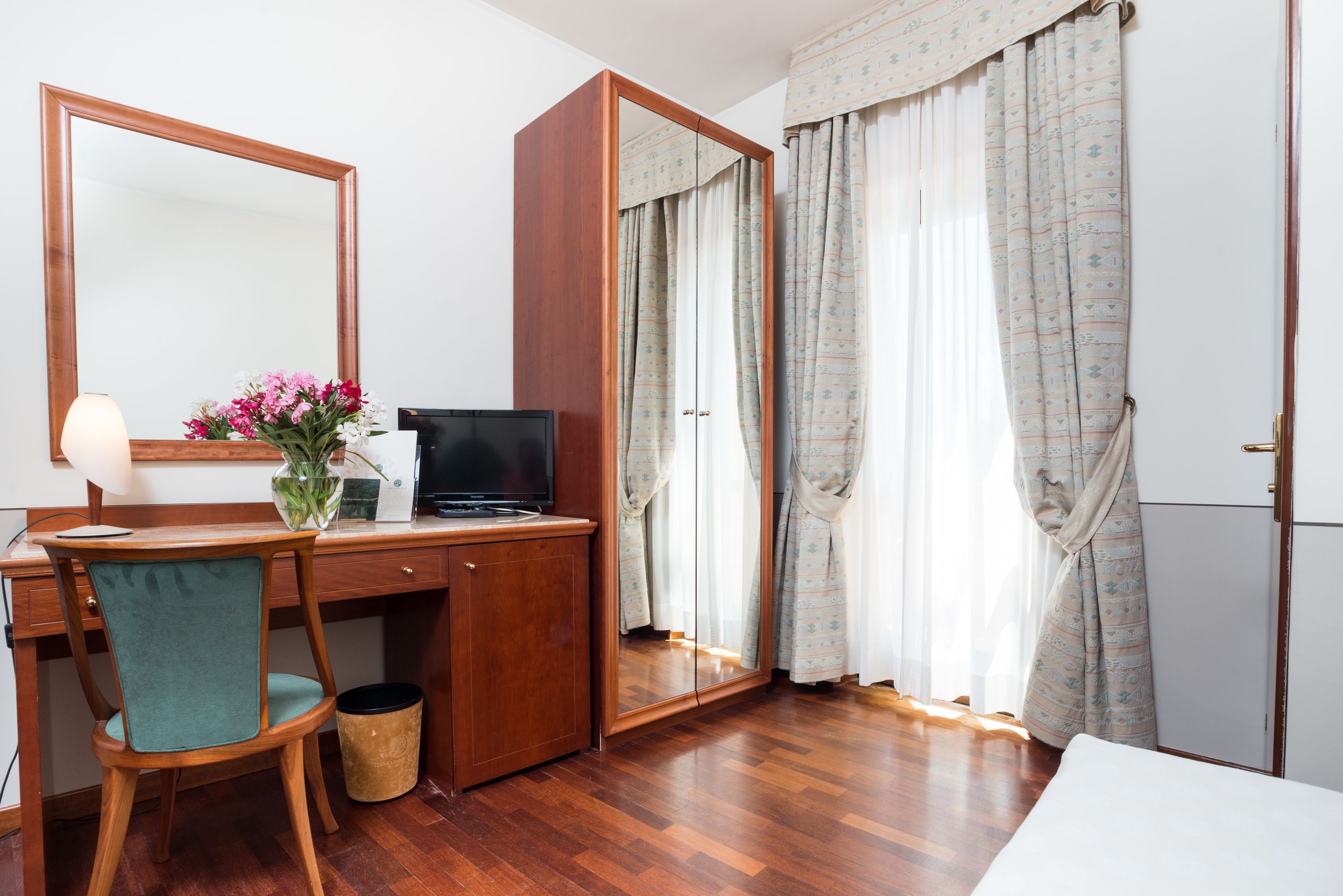 Une chambre d’hôtel avec un bureau en bois, une chaise, une télévision, un miroir et une armoire.