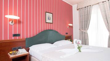Una camera d'albergo con una parete a righe rosa, una testiera verde, un comodino con un telefono e un bouquet di fiori sul letto.