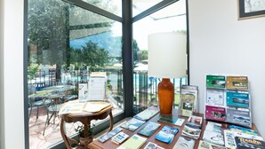 Una habitación con ventanas amplias, una mesa con folletos, una lámpara y una silla.