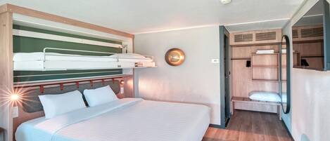 Une chambre d’hôtel avec un lit superposé, une table de chevet, un miroir et une armoire.