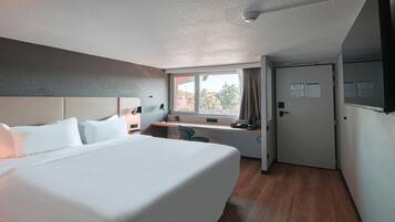 A hotel room with a bed, desk, and window.