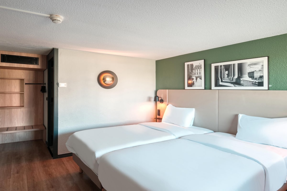 Une chambre d’hôtel avec un lit, une table de chevet avec une lampe, un tableau accroché au mur et une armoire en bois.