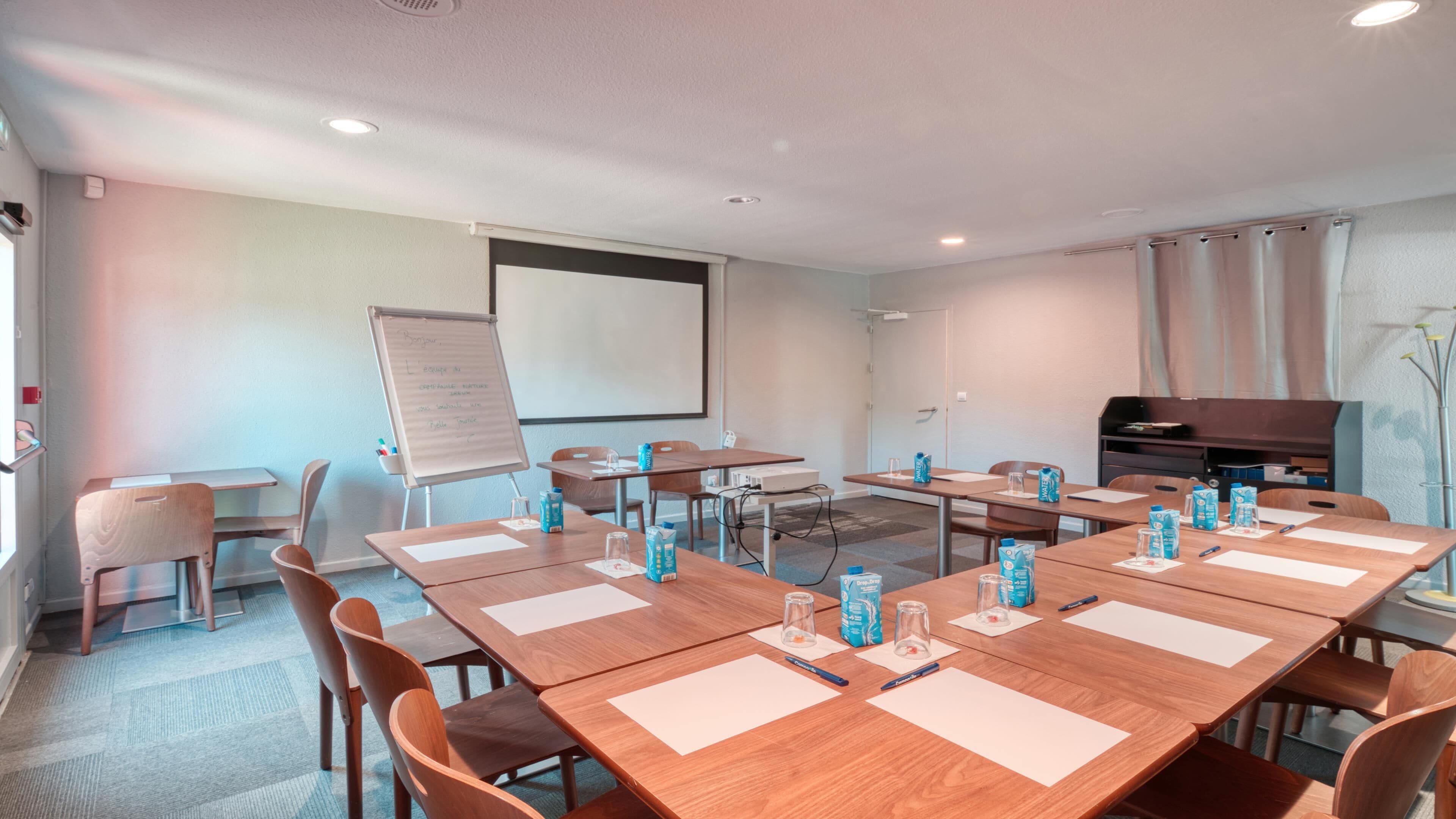 A conference room with wooden tables, chairs, a whiteboard, and a projector screen.